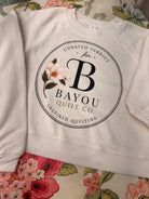 Bayou Quilt Co. women's raglan pullover fleece in Vintage White with round seal logo